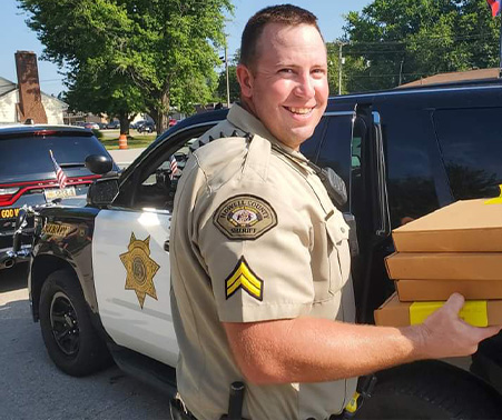 Matt Roberts holding boxes in front of his HCSO patrol car