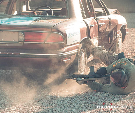 Matt Roberts laying next to a vehicle shooting a rifle during SWAT training