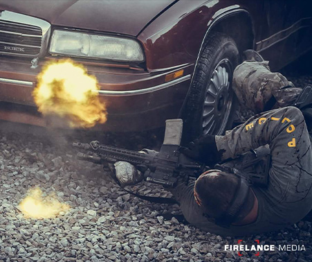 Matt Roberts laying next to a vehicle shooting a rifle during SWAT training